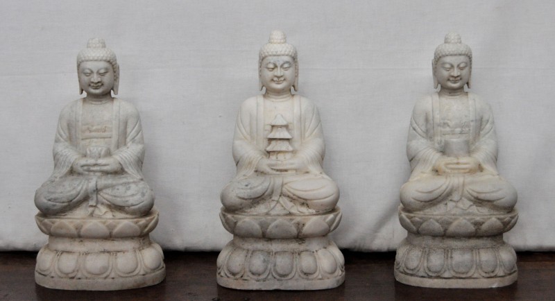 Drie zittende Boeddha’s van witte marmer. Handen in Dhyana Mudra, telkens met een ander voorwerp. Chinees werk.