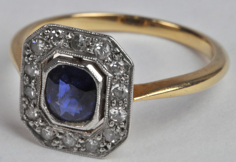 Een 18 karaats wit en geel gouden ring bezet met diamanten met een gezamenlijk gewicht van ± 0,30 ct. en een centrale saffier van ± 0,50 ct.