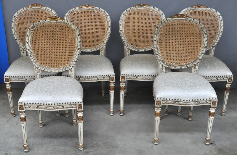 Een serie van zes stoelen van wit- en goudgepatineerd hout in Lodewijk XVI-stijl met cannage in de rug en fluwelen zit.