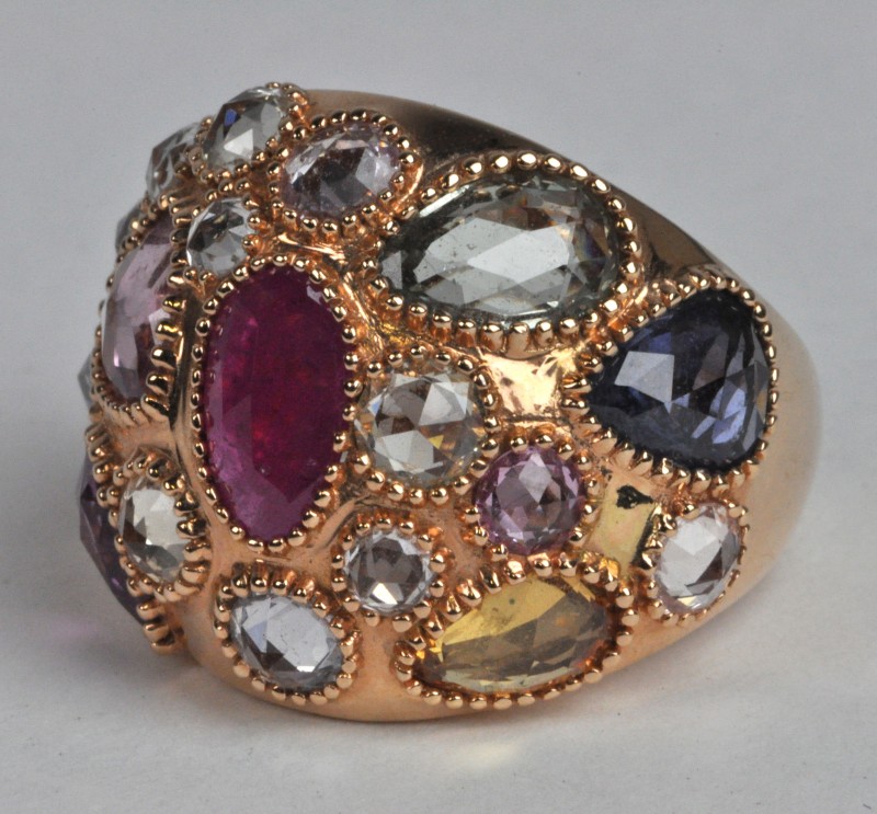 Een 18 karaats rooskleurige gouden ring bezet met verschillende kleuren saffier met een gezamenlijk gewicht van ± 9 ct. en een centrale robijn van ±  1.30 ct.