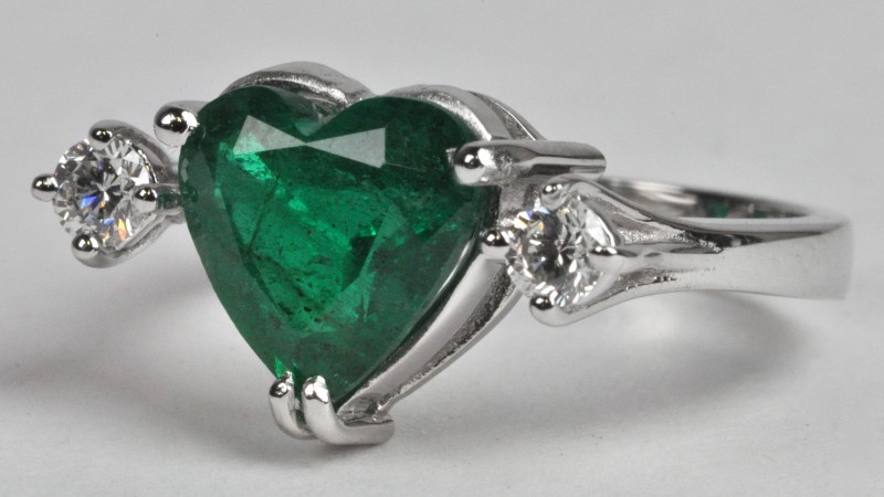 Een 18 karaats wit gouden ring bezet met diamanten met een gezamenlijk gewicht van ± 0,20 ct. en een centrale hartvormige smaragd van ± 2,10 ct.