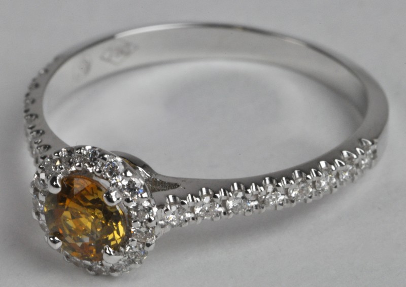 Een 18 karaats wit gouden ring bezet met diamanten met een gezamenlijk gewicht van ± 0,25 ct. en een centrale gele saffier van ± 0,54 ct.