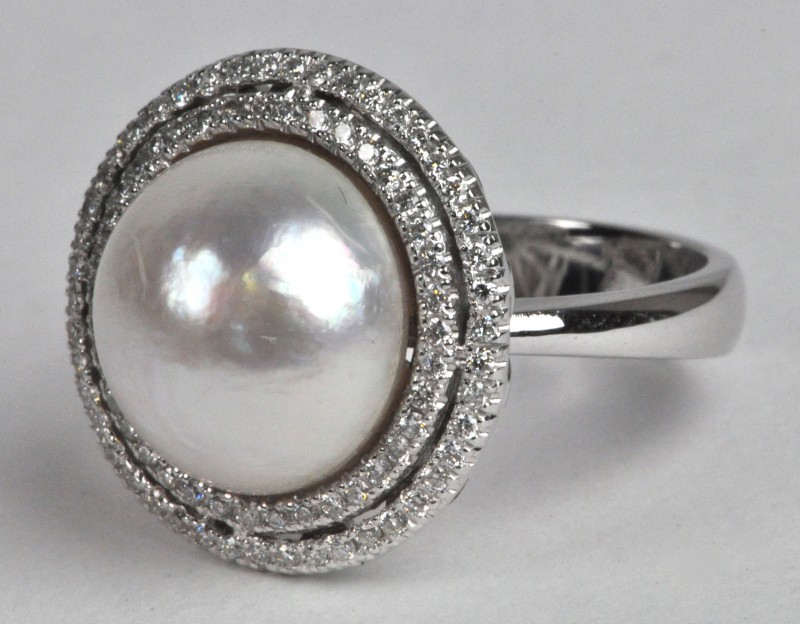 Een 18 karaats wit gouden ring bezet met diamanten met een gezamenlijk gewicht van ± 0,40 ct. en een ronde parel.