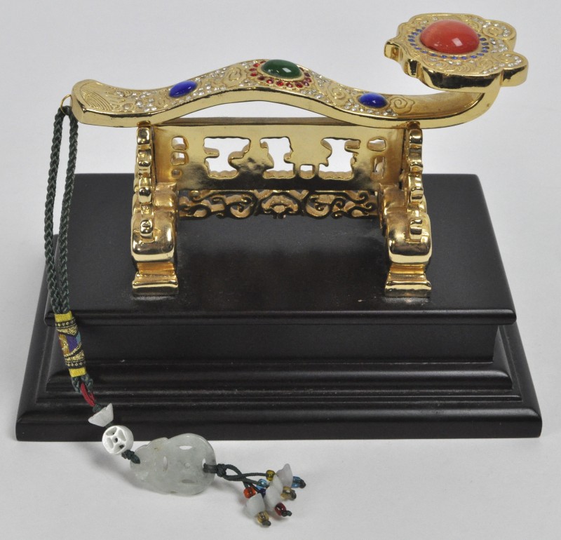 Een Chinese ruyi scepter van brons, versierd met fantasiestenen en op een houten sokkel.