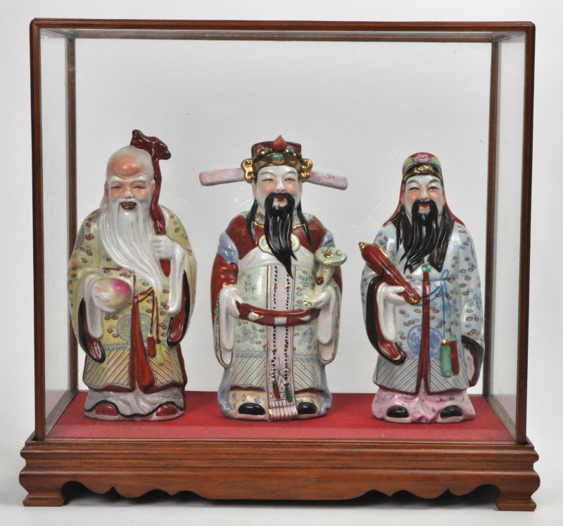 Drie Chinese wijzen van meerkleurig porselein in een een glazen presenteervitrine.
