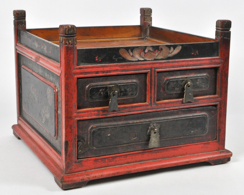 Een Chinees koffertje van gepolychromeerd hout met twee kleine laden boven een grote en versierd met een bloemendecor.