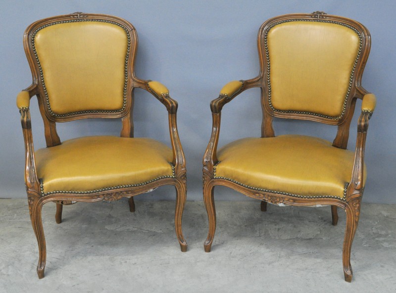 Een paar fauteuils in Lodewijk XV-stijl van gesculpteerd notenhout bekleed met okergeel leder.