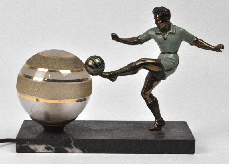 Een art deco lampje op zwart marmeren sokkel met een bolvormig glazen kapje en versierd met een bronzen voetballer.