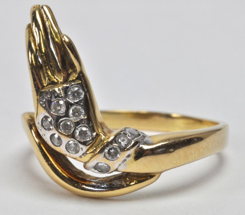 Een 18 karaats wit en geel gouden ring in de vorm van een hand bezet met fantasiestenen.