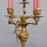 Een klokstel van verguld brons in Lodewijk XV-stijl bestaande uit een pendule en twee kandelaars met vijf lichtpunten. Met slinger en sleutel.