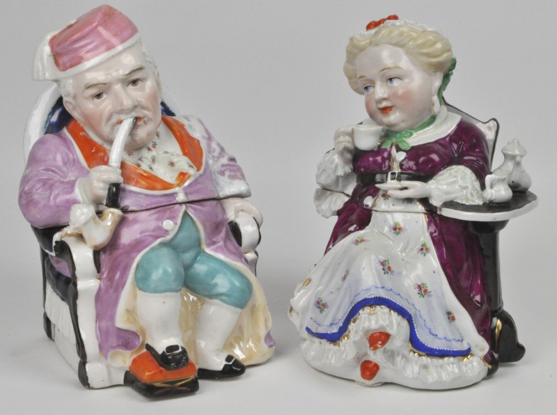 Twee tabakspotten van meerkleurig porselein in de vorm van een een pijprokende man en een theedrinkende vrouw. Engels werk.