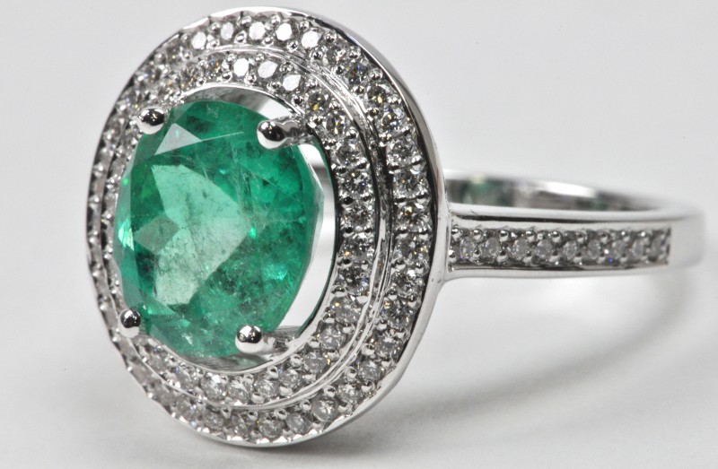 Een 18 karaats wit gouden ring bezet met diamanten met een gezamenlijk gewicht van ± 0,55 ct. en een centrale smaragd van ± 2,22 ct.