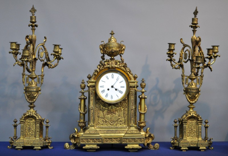 Een driedeligklokstel van geel koper in Napoléon III-stijl bestaande uit een pendule en twee kandelaars met telkens zes lichtpunten.