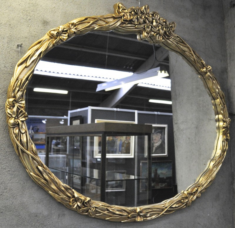 Een ovale spiegel met vergulde lijst, versierd met bloemenmotief in reliëf.