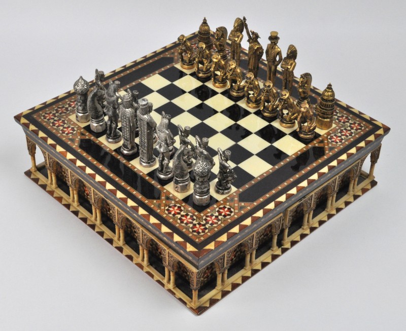 Schaakspel in een houten en kunststoffen doos met referenties naar het Alhambra. De stukken van gegoten metaal in goud-en zilverkleur stellen Amerikaanse en Russische figuren voor. Ter gelegenheid van het kampioenschap tussen Fischer en Karpov in 1975. Spaans werk.