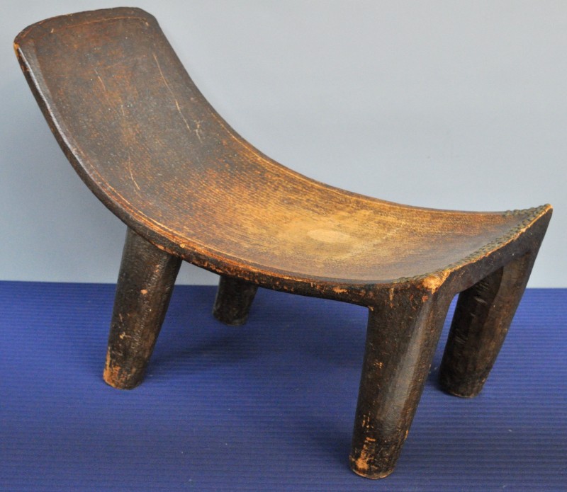 Een Afrikaanse stoel van gesculpteerd exotisch hout en sober versierd met koperen klinknagels.
