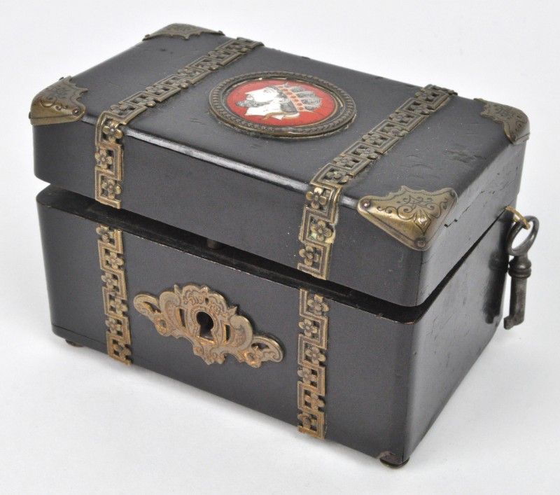 Een miniatuur reiskoffertje van zwartgelakt hout met bronsbeslag en op het deksel een ivoren plaquette met een afbeelding van een gekroond hoofd. Met sleutel. XIXde eeuw.