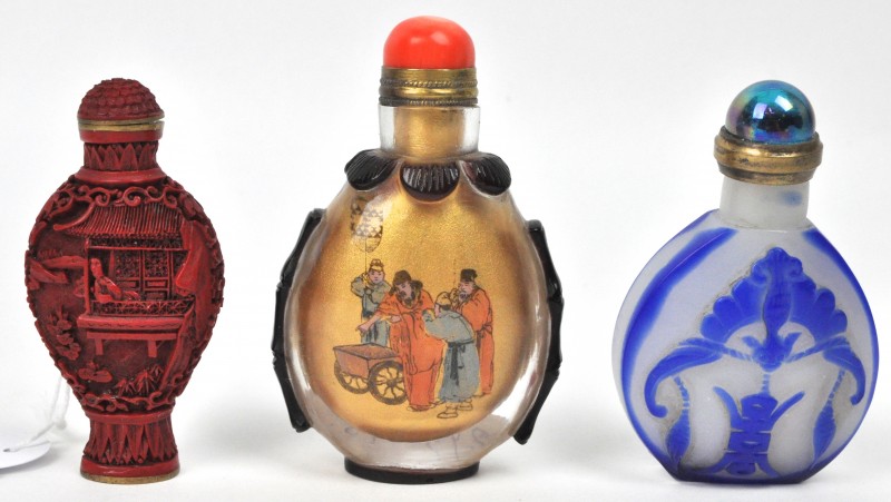 Een lot van drie Chinese snuffbottles, waarvan één van gestoken rode lak op brons, één van doorschijnend glas met églomisé en één van glaspasta, versierd met een vleermuis in reliëf.