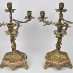 Eeen driedelig klokstel van verguld koper in Lodewijk XV-stijl, bestaande uit een pendule en twee kandelaars op onyxen sokkels.