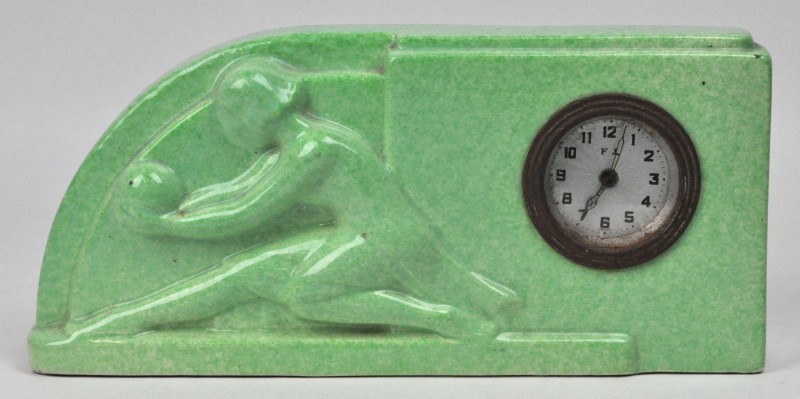 Een klokje van groen aardewerk met een afbeelding van een dame. De wijzerplaat gemerkt. ‘F J’. Tijdperk art deco.