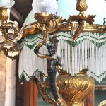 Een luchter van verguld brons in barokke stijl met en centrale glazen coupe en vijftien kleine lichtarmen, waarvan drie gedragen door saters.