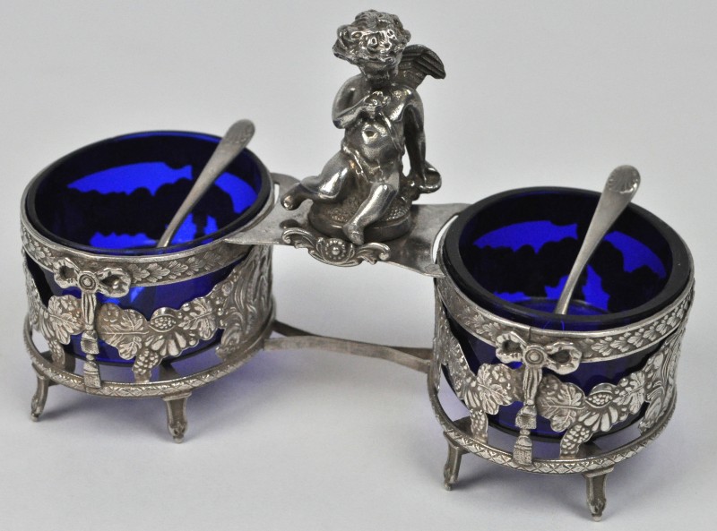 Een peper en zoutvaatje van blauw glas in een zilveren houder, bovenaan versierd met een engeltje. Met twee zilveren lepeltjes