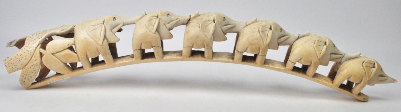 Een gesculpteerde ivoren slagtand in de vorm van  zeven olifantjes. Beschadiging. Afrikaans werk.