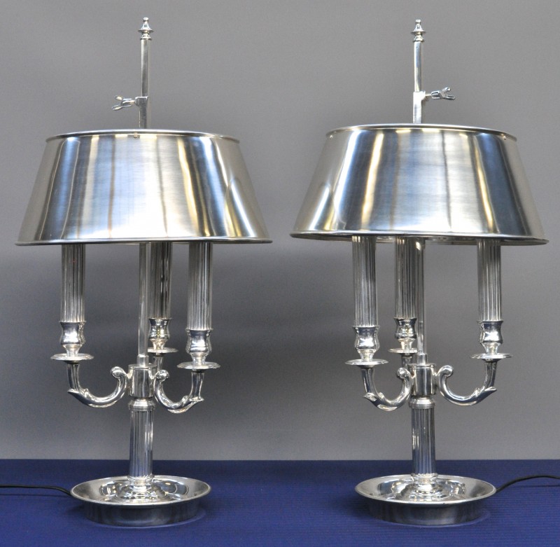 Een paar wandlampen van verzilverd metaal, inclusief de lampenkappen, in de vorm van kandelaars.
