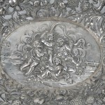 Een zilveren schaal met een geäjoureerd decor van vogels en vruchten in de vleugel en een tafereel met putti in het plat. Merken vervaagd. 800 ‰.