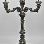 Een paar zilveren kandelaars met drie armen in barokke stijl. Belgisch importmerk van tussen 1831 en 1868. Gemerkt met ‘D’ (Delheid?).