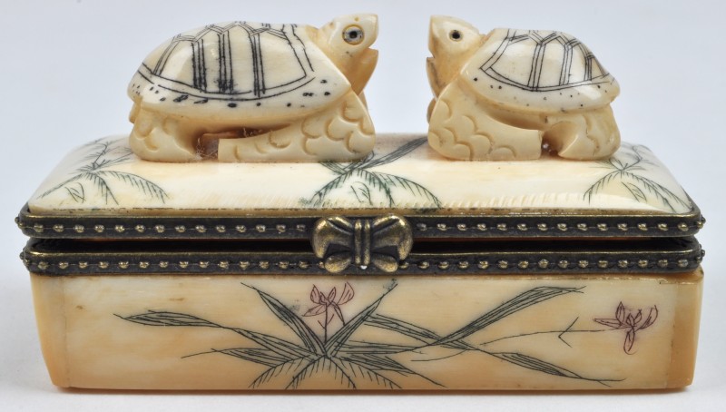 Een ivoren pillendoosje met twee gesculpteerde schildpadjes op het deksel.