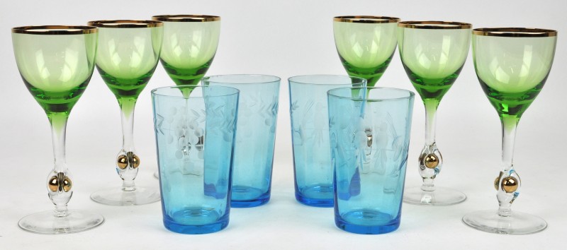 Een reeks van zes wijnglazen van groen krista met vergulde rand, de voet versierd met een verguld balletje. We voegen er vier glazen van blauw halfkristal met een geslepen decor aan toe.