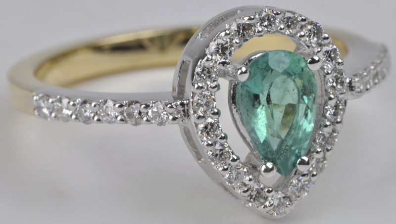 Een 18 karaats wit en geel gouden ring bezet met diamanten met een gezamenlijk gewicht van ± 0,44 ct. en een druppelvormige smaragd van ± 0,50 ct.