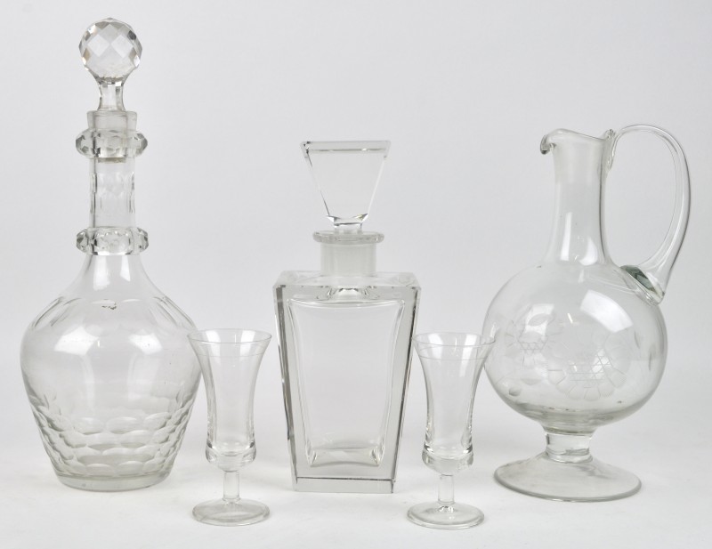 Twee verschillende glazen karaffen, waarvan één zonder stop en een vierkante van kristal met twee likeurglaasjes. De laatste beschadigd.