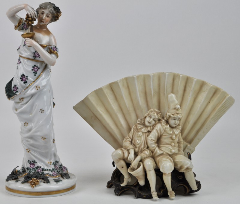 Een lot porselein, bestaande uit een meerkleurig beeldje van een dame met druiven en een siervaasje van twee zittende pierrots voor een waaier.