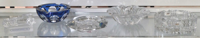 Een lot van vier verschillende kristallen asbakken, waarvan drie van Val St. Lambert en één Boheems. We voegen er een model van een Duesenberg van gegoten kristal aan toe. Gemerkt van Goebel.