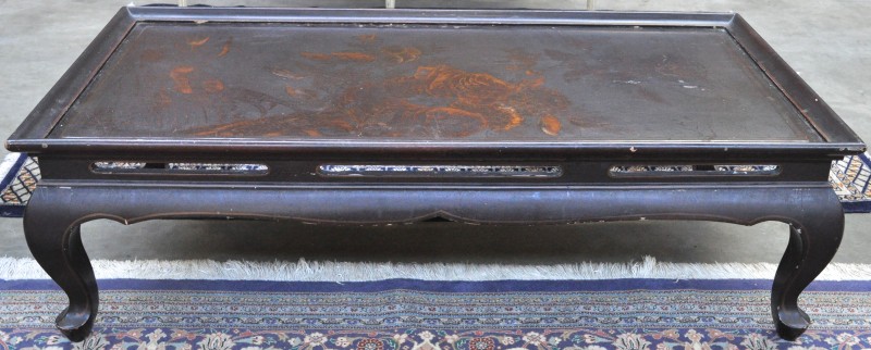 Een salontafel van bruingepatineerd hout met een rozendecor in het blad.