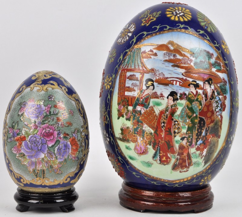 Twee verschillende eieren van Japans porselein. Het grootste met een meerkleurig decor van geisha’s in cartouches.
