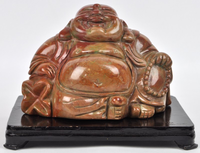 Een zittende Boeddha van speksteen op een houten voetstuk.