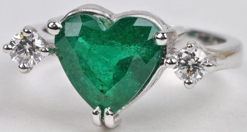 Een 18 karaats wit gouden ring bezet met diamanten met een gezamenlijk gewicht van ± 0,23 ct. en een hartvormige smaragd van ± 2,10 ct.
