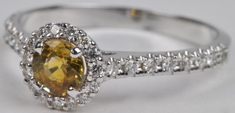 Een 18 karaats wit gouden ring bezet met diamanten met een gezamenlijk gewicht van ± 0,25 ct. en een gele saffier van ± 0,54 ct.