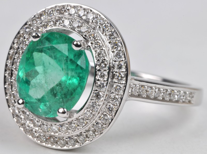 Een 18 karaats wit gouden ring bezet met diamanten met een gezamenlijk gewicht van ± 0,55 ct. en een smaragd van ± 2,20 ct.