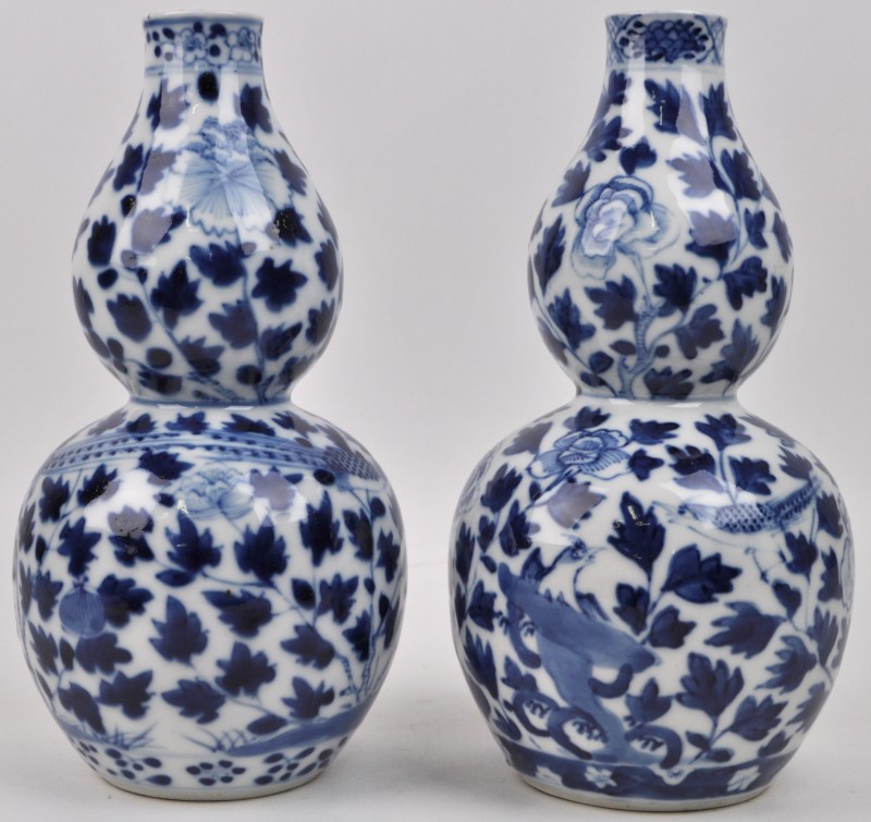 Paar kalebasvormige vazen van blauw en wit porselein met een licht verschillend bloem-en bladmotief met paradijsvogels. Chinees werk, onderaan een merk met vier tekens, refererend naar Keizer Kanghsi.