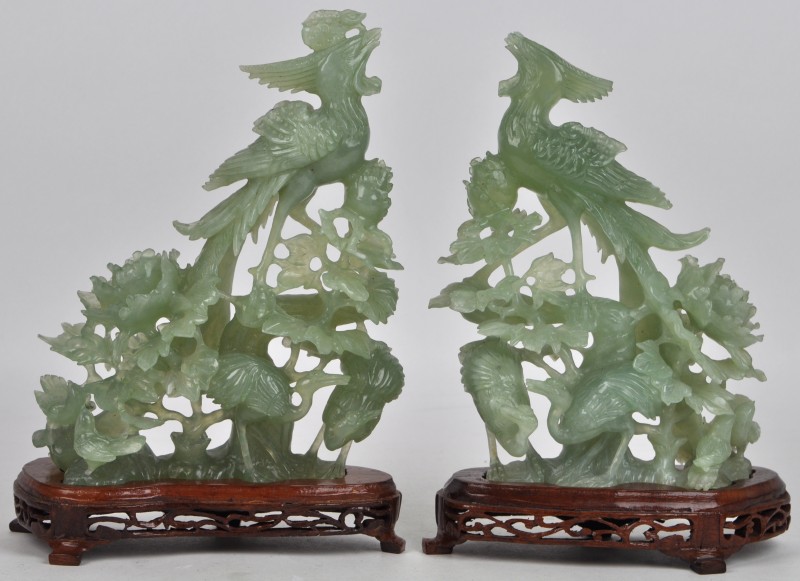 Een paar beeldjes van jade met voorstelling van twee Feng Huang of feniksen. Op hun houten sokkeltjes. Eén exemplaar met kleine herstellingen. Chinees werk.