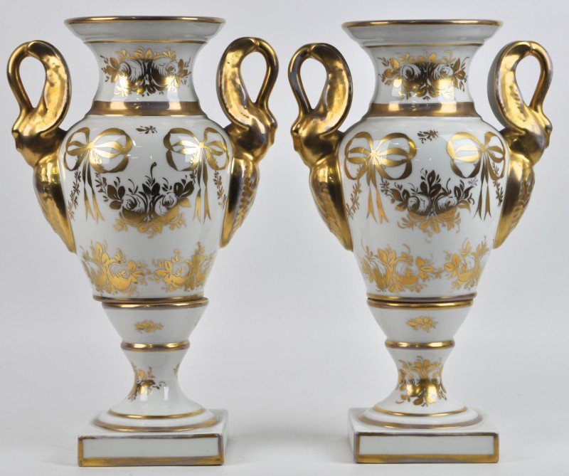 Een paar vazen van wit porselein met vergulde bloem-en strikmotieven. Oren in de vorm van zwanen. Tijdperk Empire.