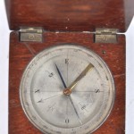 Een koperen horlogehouder in de vorm van een hondje, vier horloges, een oud kompas, een reiswekker en een thermometer met een tinnen montuur.