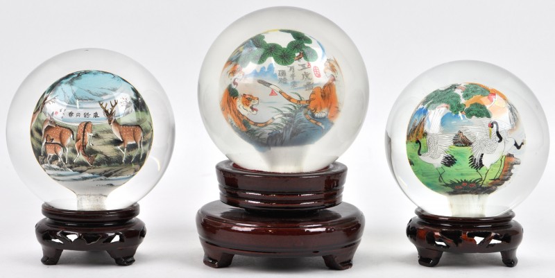 Drie glazen bollen met geschilderd interieur met dierenmotieven. Chinees werk. Met hun houten sokkeltjes.