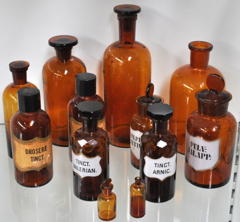 Een lot van twaalf apothekersflessen van amber gekleurd glas in diverse uitvoeringen.