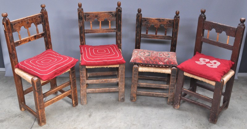 Vier stoelen van gesculpteerd eikenhout in volkse stijl met gevlochten rieten zit.