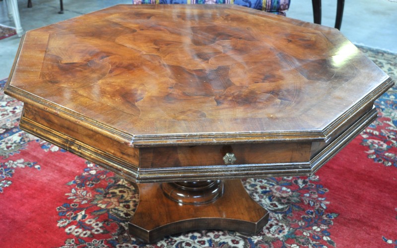 Een achthoekige salontafel van gefineerd hout op centrale poot.